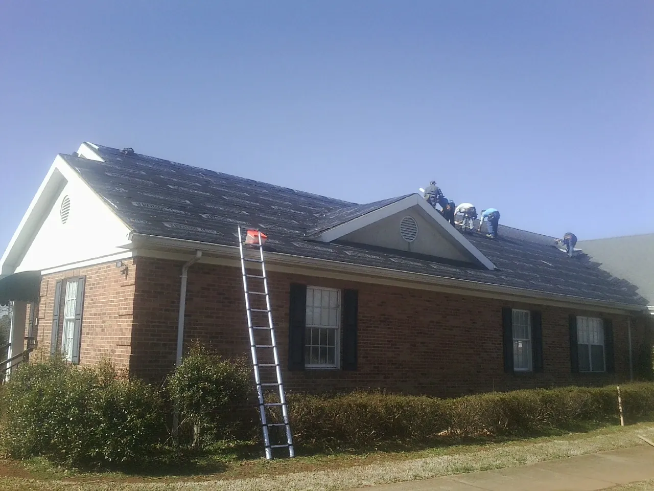 Crew tearing shingles off a brick ranch roof with a ladder set — Metal Roof Repair work by our crew in Plantsville