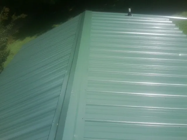 New green metal panels meeting at the ridge of a roof — Flat Roof Repair work by our crew in Plantsville