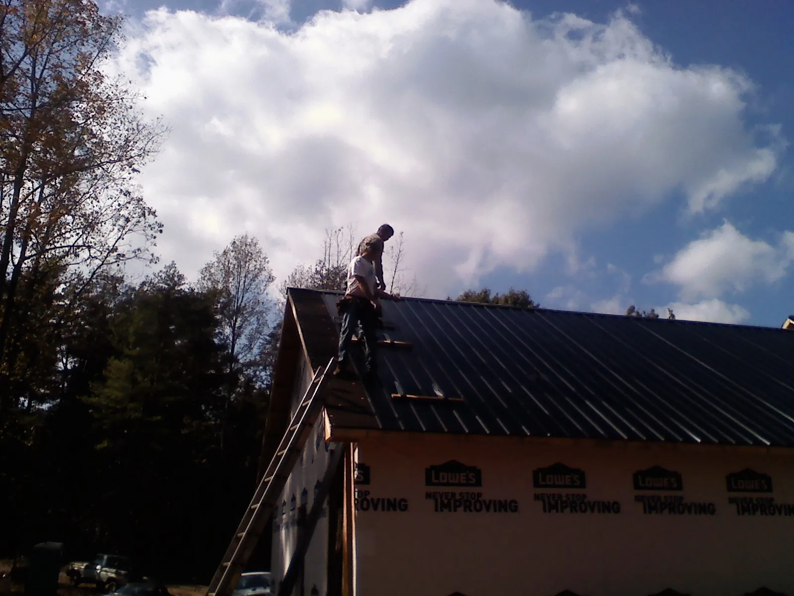 Roofer fastening dark metal panels high against a cloudy sky, from a Roof Inspection job in Plantsville