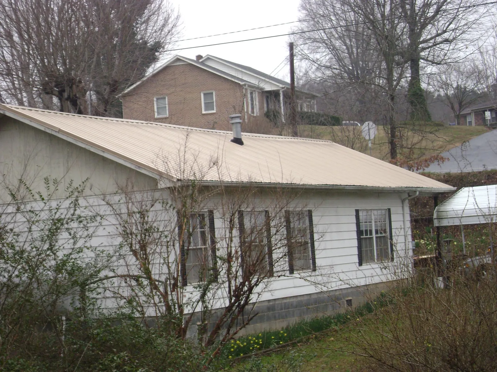 Tan metal roof on a white sided house set into a hillside — Commercial Roofing by Roofing Brothers in Plantsville